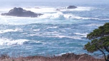 Kayalık okyanus plajı. Büyük dalgalar kayalıklara çarpıyor, mavi su sıçrıyor, deniz köpüğü. Big Sur yakınlarında doğanın gücü, 17 millik yol. Dramatik deniz manzarası. Point Lobos, Monterey, California sahili, ABD