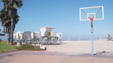 Palmiye ağaçları ve basketbol sahası veya Kaliforniya sahillerindeki saha, ABD. Sahilde sokak topu sahası ve cankurtaran durağı, ot istasyonu. Mission Sahili, San Diego. Hoop, sedye ve gökyüzü.