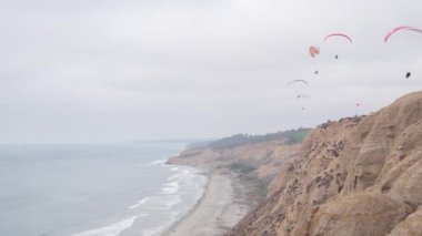 İnsanlar yamaç paraşütü yapıyor, Torrey Pines uçurumu ya da blöf. Paraglider gökyüzünde süzülüyor, paraşütle, uçurtmayla veya kanatla uçuyor. Eğlence amaçlı spor hobisi. Okyanus kıyısı, San Diego, Kaliforniya ABD. Paraşüt uçuşu