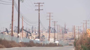 Kaliforniya, ABD 'de petrol sahasında pompalı valeleri olan kuyular. Petrol sahasında çalışan ham fosil çıkarma ekipmanları. Endüstriyel arazi, çöl vadisindeki raylar. Petrol kuyularında pompalayan birçok pompa platformu.