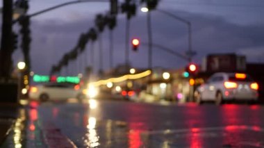 Yağmurlu havada araba ışıkları yola yansıyor. ABD 'deki şehir caddesindeki ıslak asfalta yağmur damlaları, kaldırıma düşen yağmur damlaları. Palmiye ağaçları ve yağmur, alacakaranlık. Okyanus Sahili, Kaliforniya.
