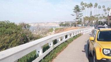 Rıhtım ya da palmiye ağaçlarıyla dolu bir sahil yolu. Sarı araba ve palmiye ağaçları, La Jolla 'daki Rocky Point, San Diego, Kaliforniya sahili, ABD. Yaz tropik tahta kaldırım estetiği. Waterside City Caddesi.