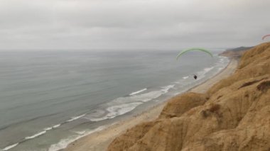İnsanlar yamaç paraşütü yapıyor, Torrey Pines uçurumu ya da blöf. Paraglider gökyüzünde süzülüyor, paraşütle, uçurtmayla veya kanatla uçuyor. Eğlence amaçlı spor hobisi. Okyanus kıyısı, San Diego, Kaliforniya ABD. Paraşüt uçuşu