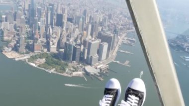 New York City 'nin kapıları helikopter uçuşuna kapalı. Helikopter Manhattan' ın üzerinde uçuyor. Dünya Ticaret Merkezi. Ayaklar spor ayakkabılarda, turist bacakları, ayakkabılar selfie pov. Amerika 'ya uçuk seyahat. Kamera sallanıyor..