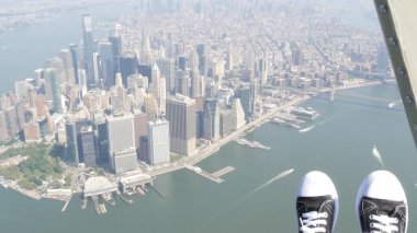 New York City 'nin kapıları helikopter uçuşuna kapalı. Helikopter Manhattan' ın üzerinde uçuyor. Dünya Ticaret Merkezi. Ayaklar spor ayakkabılarda, turist bacakları, ayakkabılar selfie pov. Amerika 'ya uçuk seyahat. Kamera sallanıyor..
