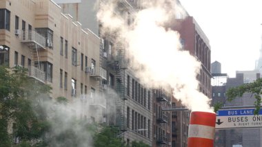 New York caddesinde buhar sızıntısı, turuncu buhar borusu yığını. Pipo dumanı. Con Edisons Buhar Operasyonları Sistemi, Manhattan. Sabah ışığı, sis. Tek otobüs şeridi. Çatıdaki su kulesi tankı.
