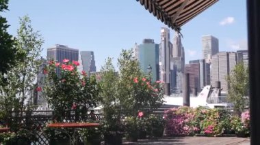 New York City rıhtımı silueti, Manhattan şehir merkezi binaları, nehir kenarındaki gökdelenler, doğu nehri suyu. Brooklyn rıhtımından deniz kenarı manzarası, çiçekler açıyor. Birleşik Devletler mimarisi.