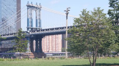 Manhattan Köprüsü 'nden Brooklyn Dumbo' ya. New York 'un sembolü, Amerika' nın seyahat yeri. Birleşik Devletler 'in mimarisi, turizm simgesi. Kablolu yayın köprüsü. Park yeşili, nehir kenarında yeşil çimen pikniği..