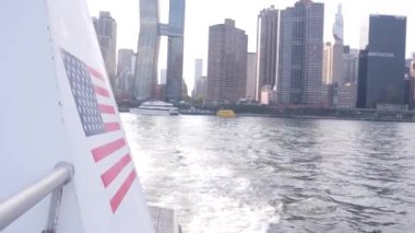 Feribottan New York City silueti. Manhattan şehir merkezindeki gökdelenler feribottan görünüyor. Doğu nehri kıyısı manzarası, nehir kıyısındaki binalar ABD 'de su kenarında. Amerikan bayrağı.