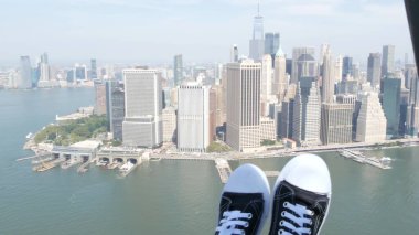 New York City 'nin kapıları helikopter uçuşuna kapalı. Helikopter Manhattan' ın üzerinde uçuyor. Dünya Ticaret Merkezi. Ayaklar spor ayakkabılarda, turist bacakları, ayakkabılar selfie pov. Amerika 'ya uçuk seyahat. Kamera sallanıyor..