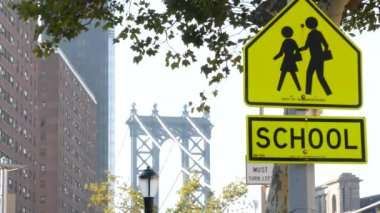 Okul bölgesi sarı yol işareti, insanlar karşıya geçiyor. Manhattan şehir merkezinde, New York City mimarisinde çocuk güvenliği. Eğitim sembolü ABD. İleride yayalar, trafik işaretleri ve Manhattan Köprüsü
