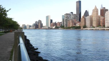 New York şehri kıyısı silueti, Manhattan şehir merkezi binaları, nehir kıyısındaki gökdelenler, doğu nehri suyu. Roosevelt Adası 'ndan deniz kenarı manzarası. Birleşik Devletler mimarisi ve gayrimenkul.