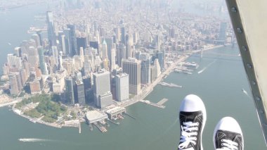 New York City 'nin kapıları helikopter uçuşuna kapalı. Helikopter Manhattan' ın üzerinde uçuyor. Dünya Ticaret Merkezi. Ayaklar spor ayakkabılarda, turist bacakları, ayakkabılar selfie pov. Amerika 'ya uçuk seyahat. Kamera sallanıyor..