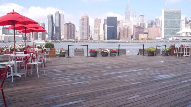 New York şehri kıyısı silueti, Manhattan şehir merkezi binaları, nehir kıyısındaki gökdelenler, doğu nehri kıyısındaki kafe şemsiyeleri. Hunters Point, Long Island, Queens, ABD 'den liman kenti manzarası.