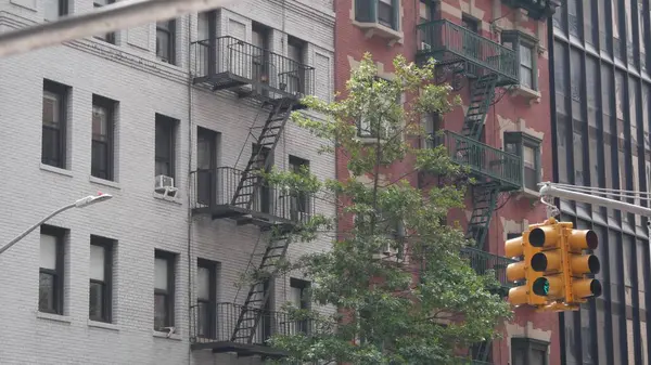 New York caddesi kavşağı, sarı trafik ışığı, ulaşım yolu kavşağı, Birleşik Devletler. Konut mimarisi. New York Emlak, yangın merdivenli kırmızı kahverengi tuğlalı ev. Manhattan.