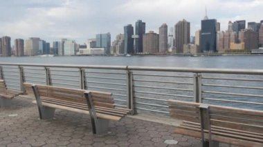 New York şehri kıyısı silueti, Manhattan şehir merkezi binaları, nehir kıyısındaki gökdelenler, doğu nehri suyu. Waterside City, Gantry Plaza Park, Long Island, Queens, ABD. Nehir kenarındaki bank.