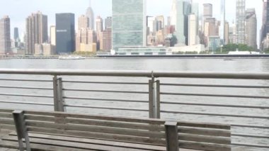 New York şehri kıyısı silueti, Manhattan şehir merkezi binaları, nehir kıyısındaki gökdelenler, doğu nehri suyu. Waterside City, Gantry Plaza Park, Long Island, Queens, ABD. Nehir kenarındaki bank.