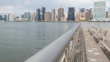 New York şehri kıyısı silueti, Manhattan şehir merkezi binaları, nehir kıyısındaki gökdelenler, doğu nehri suyu. Waterside City, Gantry Plaza Park, Long Island, Queens, ABD. Nehir kenarındaki bank.