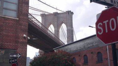 New York City Brooklyn Bridge from Dumbo. Red brick wall, old historic tobacco warehouse, Market and Theater. Low angle view. Travel United States, USA architecture. One way arrow, stop road sign. clipart