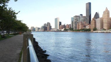 New York şehri kıyısı silueti, Manhattan şehir merkezi binaları, nehir kıyısındaki gökdelenler, doğu nehri suyu. Roosevelt Adası 'ndan deniz kenarı manzarası. Birleşik Devletler mimarisi ve gayrimenkul.