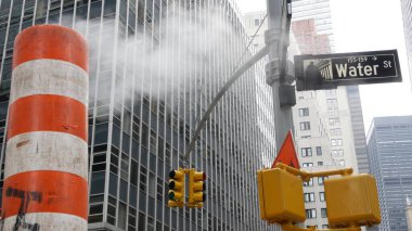 New York Su Sokağı 'nda buhar sızıntısı, turuncu buhar borusu yığını. Pipo dumanı. Con Edisons Buhar Operasyonları Sistemi, Manhattan şehir merkezi finans bölgesi mimarisi. Trafik ışığı