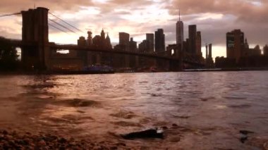 Brooklyn Köprüsü ve New York City Manhattan şehir merkezi silueti, finans bölgesi şehir manzarası. Birleşik Devletler Dünya Ticaret Merkezi gökdeleni. Waterfront Pebble Sahili, Dumbo, ABD. Dramatik gün batımı bulutlu gökyüzü