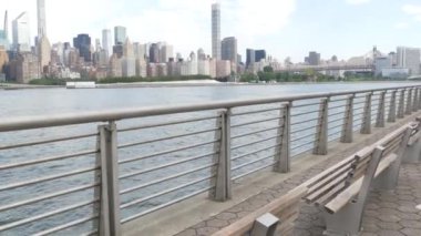 New York şehri kıyısı silueti, Manhattan şehir merkezi binaları, nehir kıyısındaki gökdelenler, doğu nehri suyu. Waterside City, Gantry Plaza Park, Long Island, Queens, ABD. Nehir kenarındaki bank.