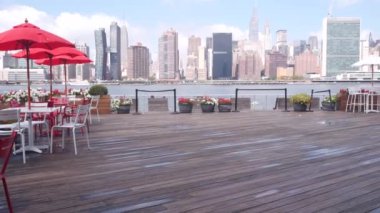 New York şehri kıyısı silueti, Manhattan şehir merkezi binaları, nehir kıyısındaki gökdelenler, doğu nehri kıyısındaki kafe şemsiyeleri. Hunters Point, Long Island, Queens, ABD 'den liman kenti manzarası.