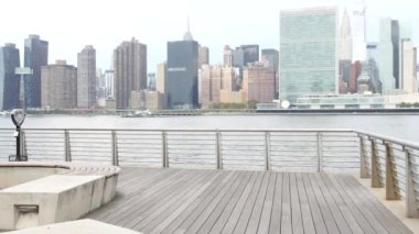 New York şehri kıyısı silueti, Manhattan şehir merkezi binaları, nehir kıyısındaki gökdelenler, doğu nehri suyu. Waterside City, Gantry Plaza Park, Long Island, Queens, ABD. Nehir kenarındaki bank.