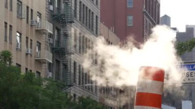New York caddesinde buhar sızıntısı, turuncu buhar borusu yığını. Pipo dumanı. Con Edisons Buhar Operasyonları Sistemi, Manhattan. Sabah ışığı, sis. Tek otobüs şeridi. Çatıdaki su kulesi tankı.
