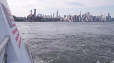 Feribottan New York City silueti. Manhattan şehir merkezinde, feribottan yükselen gökdelenler. Doğu nehri kıyısı manzarası, nehir kenarı mimarisi, Amerikan bayrağı. Empire State, Chrysler Binası.