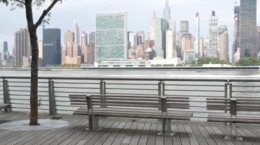 New York şehri kıyısı silueti, Manhattan şehir merkezi binaları, nehir kıyısındaki gökdelenler, doğu nehri suyu. Waterside City, Gantry Plaza Park, Long Island, Queens, ABD. Nehir kenarındaki bank.