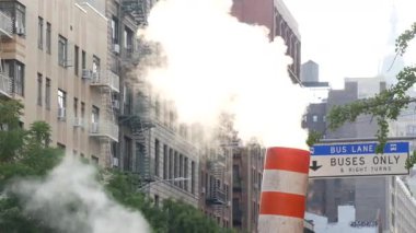 New York caddesinde buhar sızıntısı, turuncu buhar borusu yığını. Pipo dumanı. Con Edisons Buhar Operasyonları Sistemi, Manhattan. Sabah ışığı, sis. Tek otobüs şeridi. Çatıdaki su kulesi tankı.