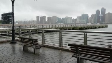 New York City rıhtım silueti, Manhattan Midtown binaları, doğu nehri kıyısında nehir kenarındaki gökdelenler. Waterside City, Gantry Plaza Park, Long Island, Queens, ABD. Nehir kenarındaki bank, yağmurlu.
