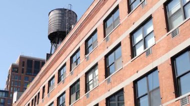 New York City klasik endüstriyel bina dış mimarisi, ABD. Tipik kırmızı tuğla, ön cephedeki pencereler. Çatıdaki su kulesi, çatıdaki tank. Mavi gökyüzü.
