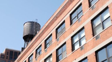New York City klasik endüstriyel bina dış mimarisi, ABD. Tipik kırmızı tuğla, ön cephedeki pencereler. Çatıdaki su kulesi, çatıdaki tank. Mavi gökyüzü.