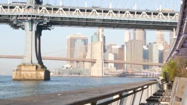 New York City Manhattan Köprüsü 'nden Brooklyn' e. Şehir merkezindeki liman kenti, 35. İskeleden ABD finans bölgesi gökdeleni. Doğu nehri ikonik manzarası, sabah gün batımı. Nehir kenarındaki bankta