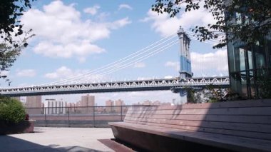 New York City Manhattan Köprüsü 'nden Brooklyn Dumbo' ya. Liman piyasasının çatısındaki bankta, Amerika Birleşik Devletleri 'nin ikonik seyahat rotası. Mavi gökyüzündeki bulutlar. New York 'un çatısında. Kablo destekli köprü, ABD.