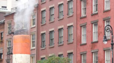 New York caddesinde buhar sızıntısı, turuncu buhar borusu yığını. Pipo dumanı. Con Edisons Buhar Operasyonları Sistemi, 5. Cadde Manhattan Midtown Mimarisi. Kırmızı tuğla ev, fener.