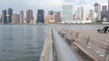 New York şehri kıyısı silueti, Manhattan şehir merkezi binaları, nehir kıyısındaki gökdelenler, doğu nehri suyu. Waterside City, Gantry Plaza Park, Long Island, Queens, ABD. Nehir kenarındaki bank.