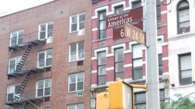 New York City kavşağı, sokak kavşağı tabelası. 6. Cadde, Americas Bulvarı köşe işareti, Midtown bölgesi, New York. Sarı trafik ışığı. Ev, kırmızı tuğla bina.