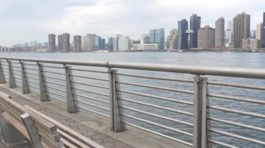 New York şehri kıyısı silueti, Manhattan şehir merkezi binaları, nehir kıyısındaki gökdelenler, doğu nehri suyu. Waterside City, Gantry Plaza Park, Long Island, Queens, ABD. Nehir kenarındaki bank.