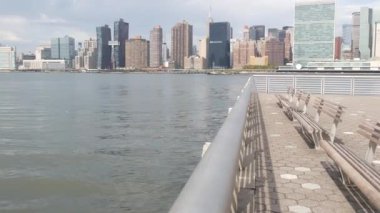 New York şehri kıyısı silueti, Manhattan şehir merkezi binaları, nehir kıyısındaki gökdelenler, doğu nehri suyu. Waterside City, Gantry Plaza Park, Long Island, Queens, ABD. Nehir kenarındaki bank.