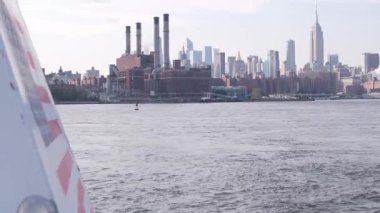 Feribottan New York City silueti. Manhattan şehir merkezinde, feribottan yükselen gökdelenler. Doğu nehri kıyısı manzarası, nehir kıyısında deniz kenarında mimari. Empire State Binası. Amerikan bayrağı.