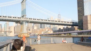 New York, Birleşik Devletler - 7 Eylül 2023: Manhattan Köprüsü. Rıhtım 35 'in yanındaki balıkçı salıncak, şehir merkezindeki deniz kenarı manzarası. Dünya Ticaret Merkezi gökdeleni, insanlar balık tutuyor ve sabah günbatımı.