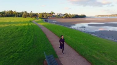 A beautiful young woman jogging in a park by the beach at low tide.