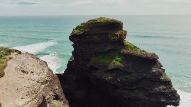 The drone footage captures stunning island peaks at Piha beach, offering a bird's eye view of the rugged and dramatic landscapes.