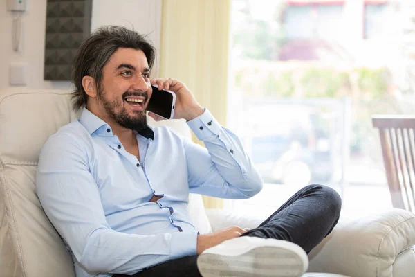 stock image Handsome young man sitting at home while talking on the phone daytime