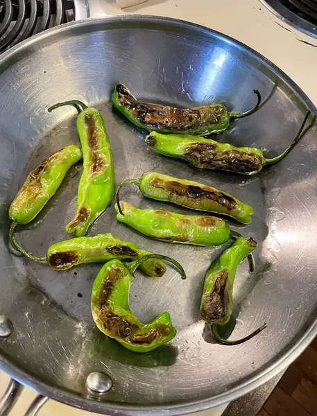 stock image An appetizer of beautiful green shishito peppers becoming blistered and flavorful in a frying pan with oil, according to a trendy recipe. 