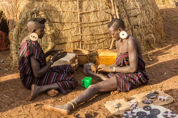stock image OMO VALLEY, ETHIOPIA - FEBRUARY 6, 2020: Mursi tribe girls preparing lip plates in their village, Ethiopia